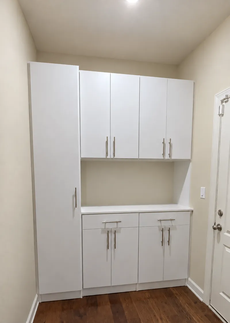 White cabinet wall with a tall cabinet, upper cabinets and a countertop niche beside a door