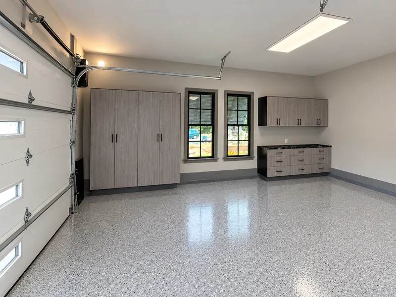 Garage with wood-grain tall cabinets, wall cabinets and a base cabinet run on an epoxy floor