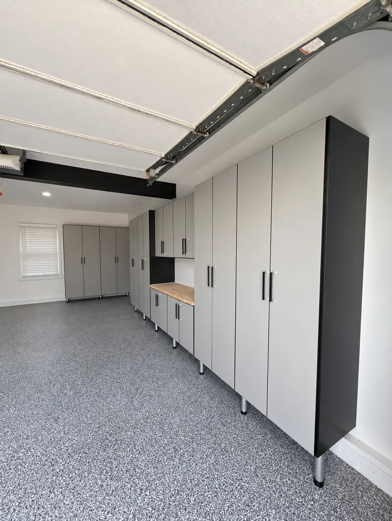 Garage with a long run of light gray tall cabinets and a butcher-block work surface on an epoxy floor