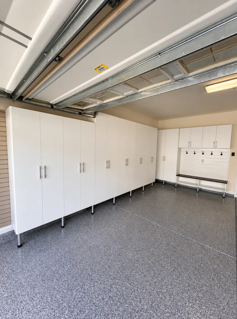 Garage with a wall of white tall cabinets and a bench with coat hooks on an epoxy floor