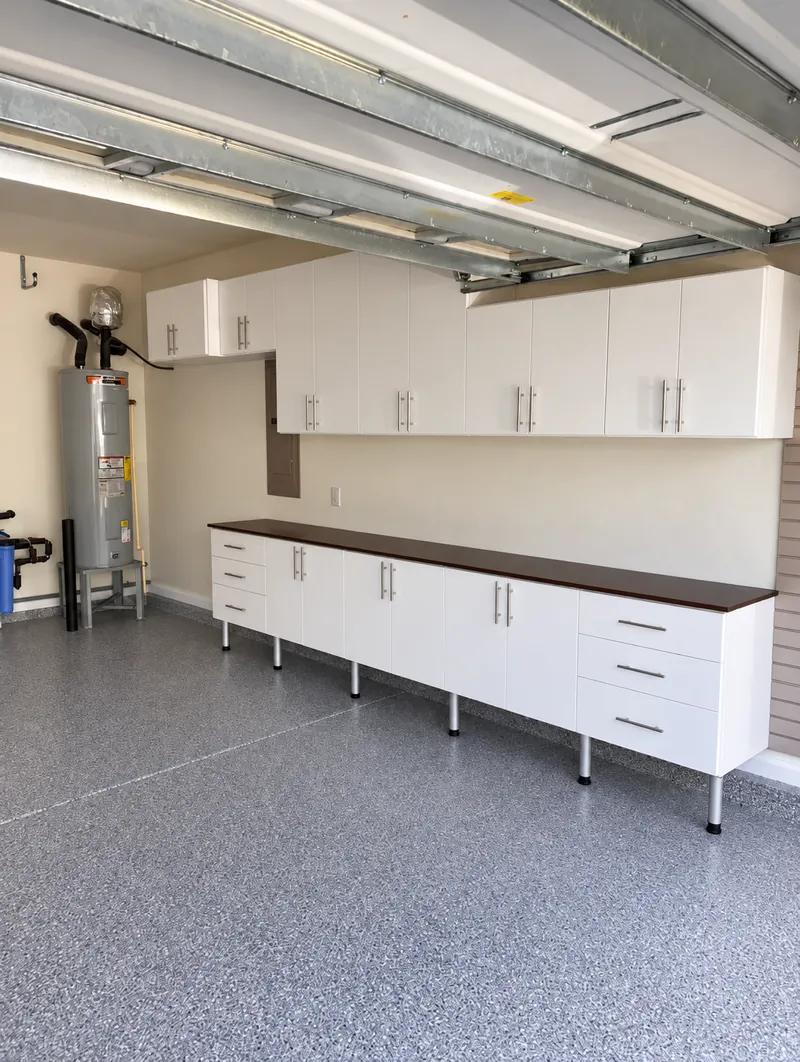 Garage with white wall cabinets above a base cabinet run with a dark countertop