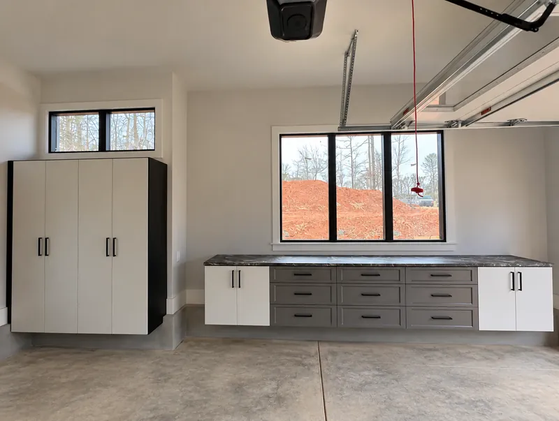 Garage with white tall cabinets and a base cabinet run with drawers and a stone countertop
