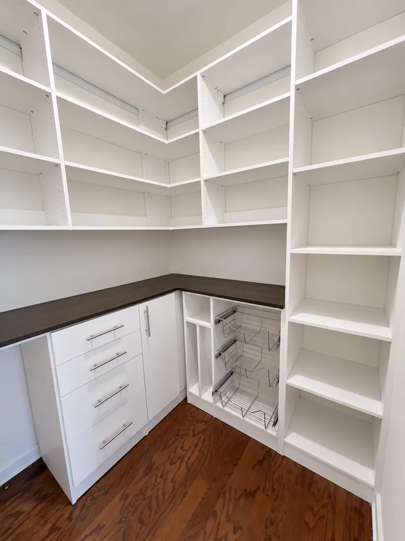 White walk-in pantry with a dark wood countertop, drawers, wire pull-out baskets and corner shelving