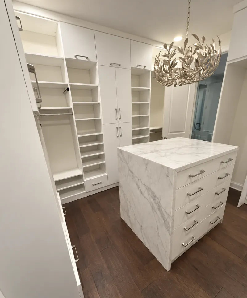 White walk-in closet with a marble waterfall island, floor-to-ceiling shelving and a leaf chandelier