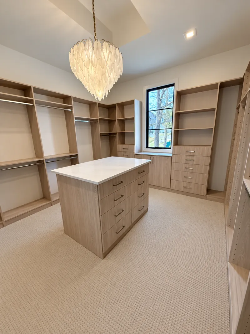 Walk-in closet in a light wood-grain finish with hanging sections, drawers and a center island