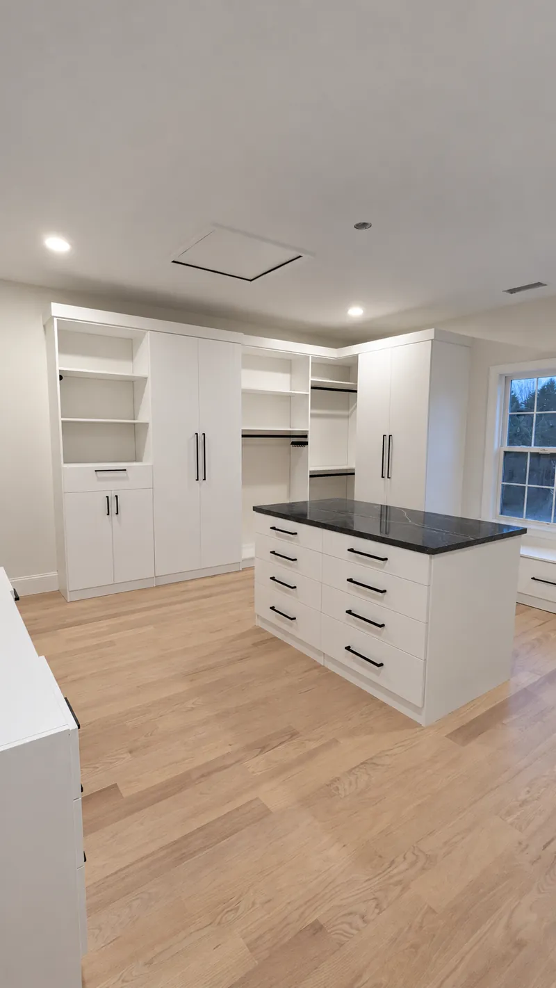 White walk-in closet with tall cabinets, open shelving and a black granite-topped island
