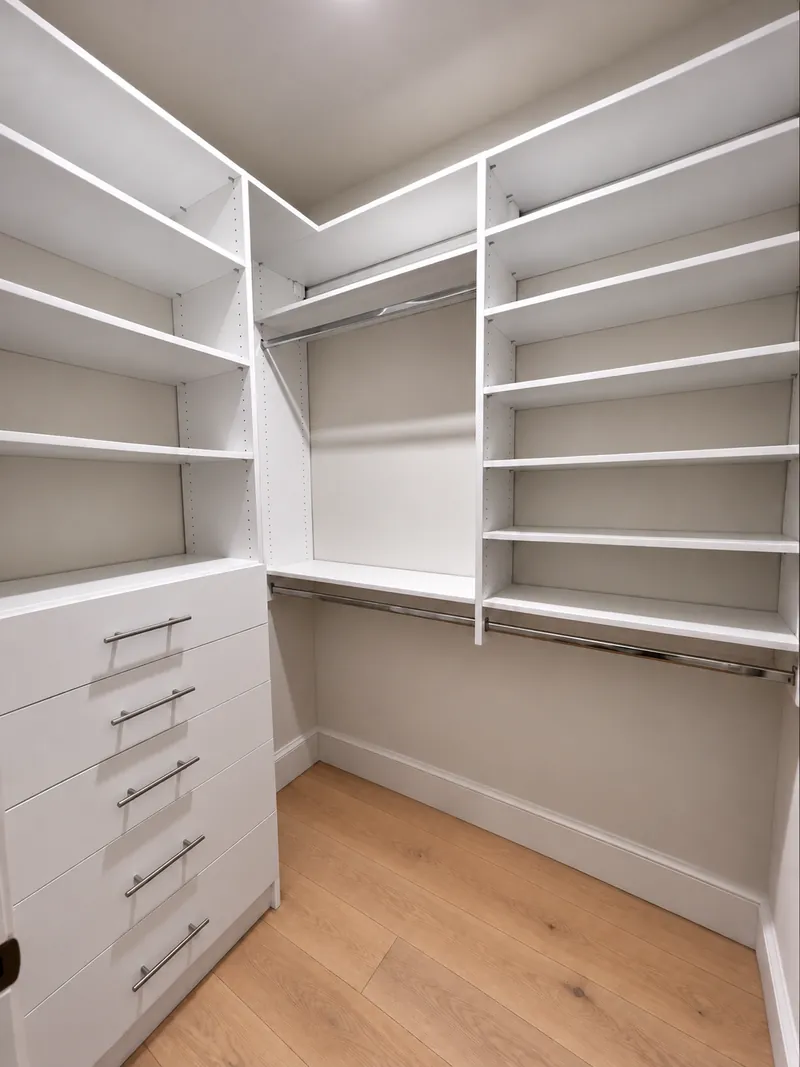 White corner walk-in closet with open shelving, double hanging rods and a drawer stack